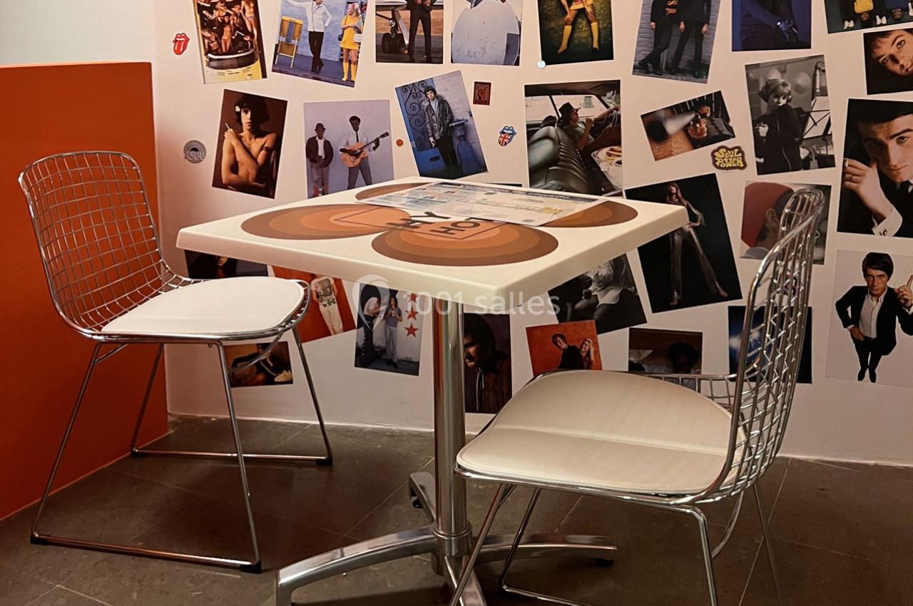 Deux chaises modernes entourent une table carrée dans un coin décoré de photos variées sur les murs.