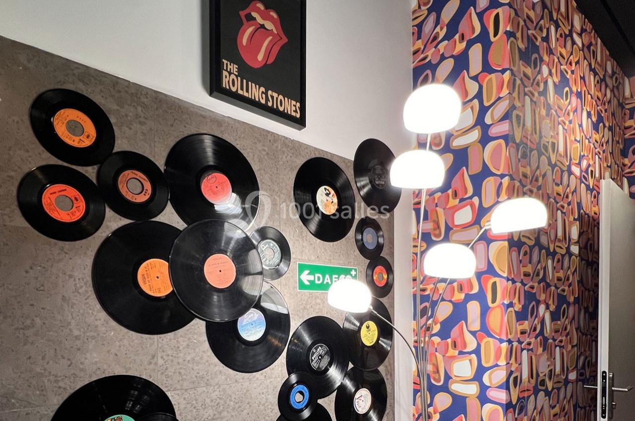 Mur décoré de vinyles et d'une affiche des Rolling Stones, éclairé par des lampes modernes et entouré d'un papier peint…