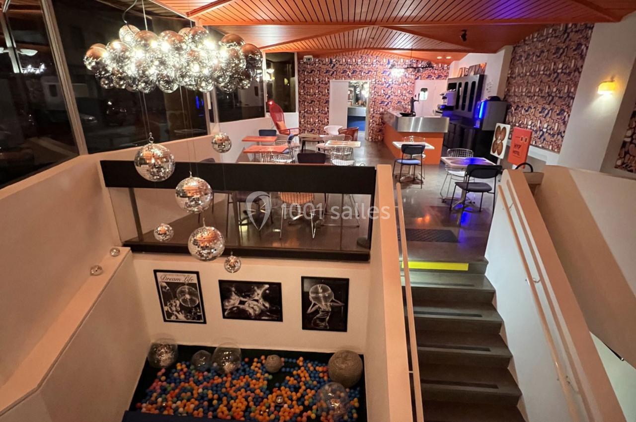 Vue d'un espace intérieur moderne avec un plafond en bois, des tables, un escalier et une piscine à balles colorées.