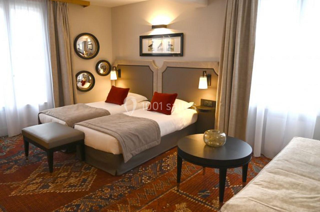 Chambre avec deux lits simples, décoration chaleureuse, tapis coloré, miroirs ronds et lumière naturelle.