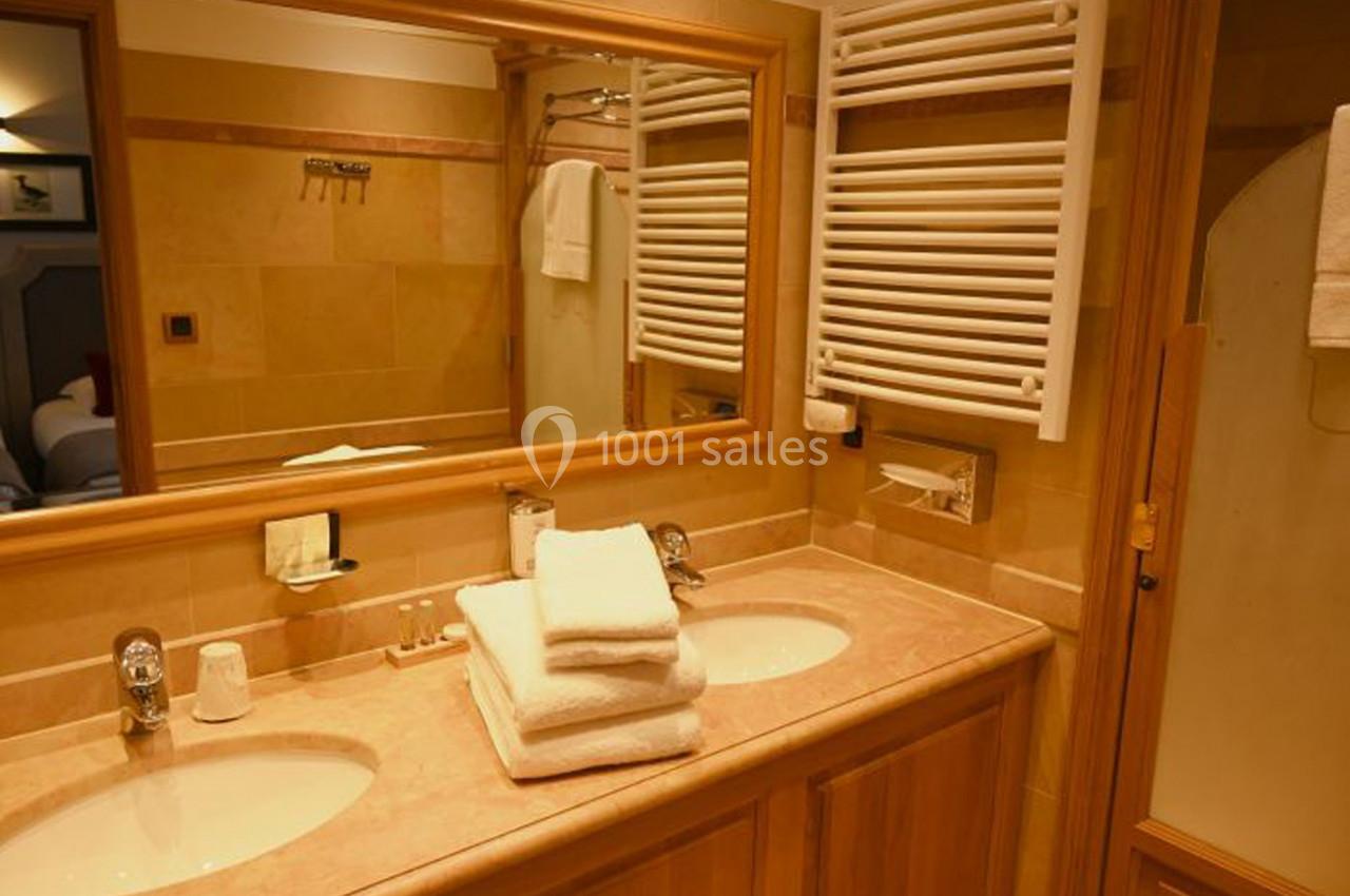 Salle de bain avec double vasque, miroir, serviettes pliées, radiateur mural et décor en tons beige.