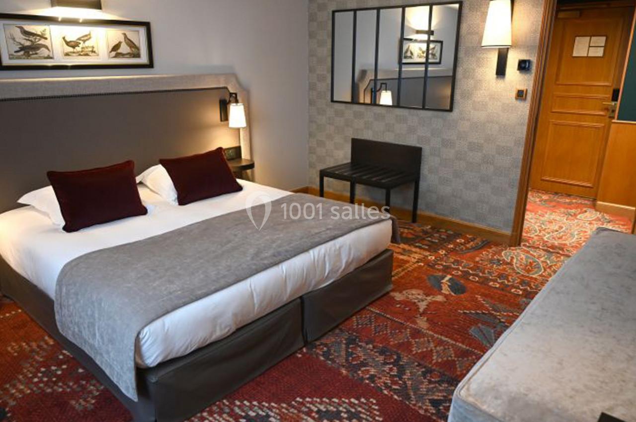 Chambre d'hôtel avec lit double, coussins rouges, éclairage doux, miroir mural et décoration chaleureuse.