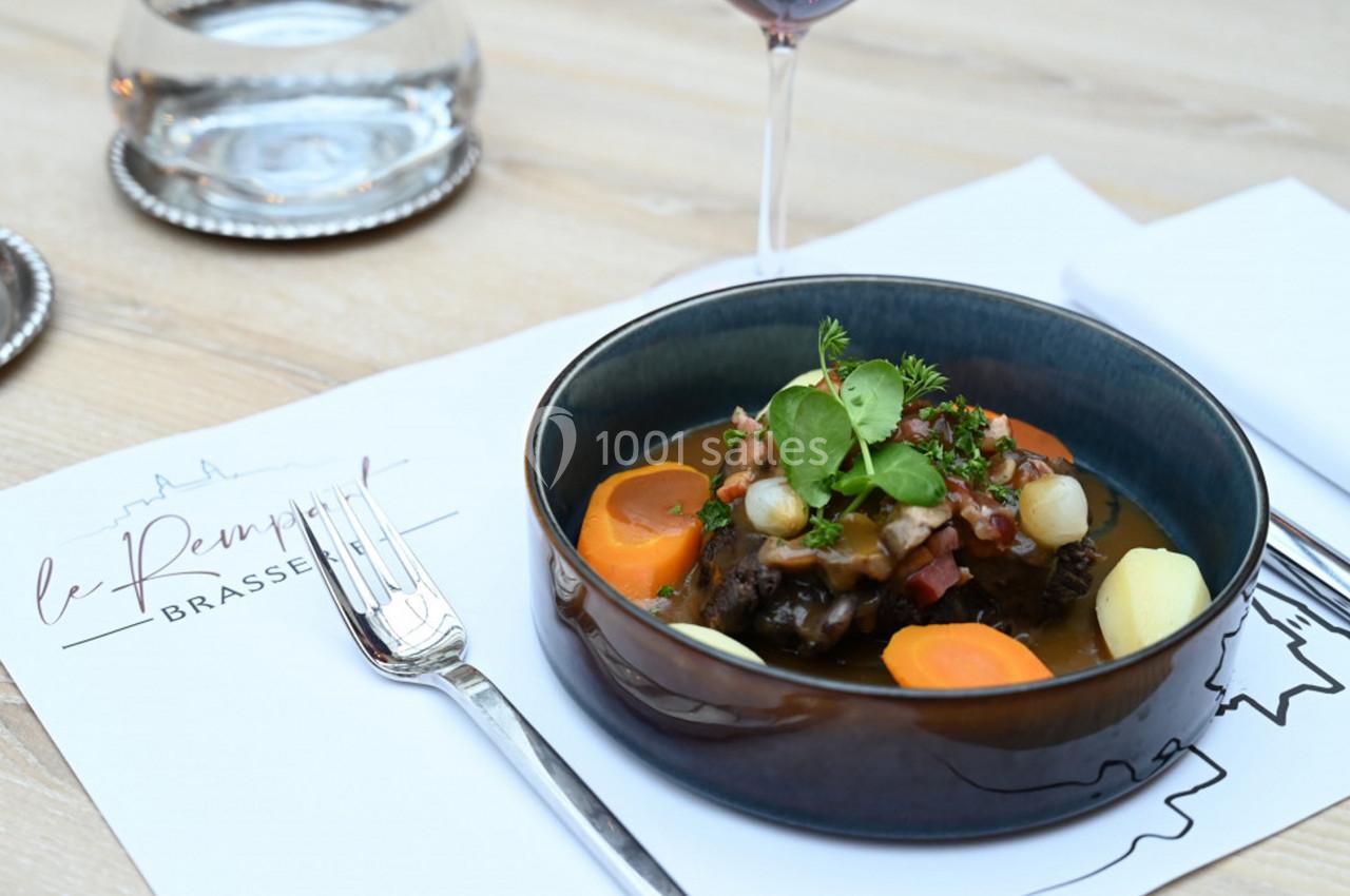 Assiette de bœuf mijoté avec légumes, servie sur une table dressée avec une fourchette et un verre de vin.