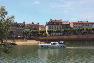 Bateau de plaisance naviguant sur une rivière bordée de maisons anciennes et d'arbres alignés.
