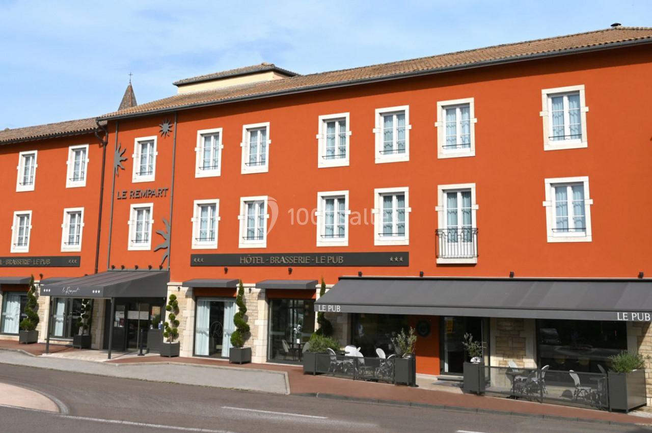 Façade d'un bâtiment rouge avec des fenêtres blanches, abritant un hôtel et une brasserie avec terrasses.