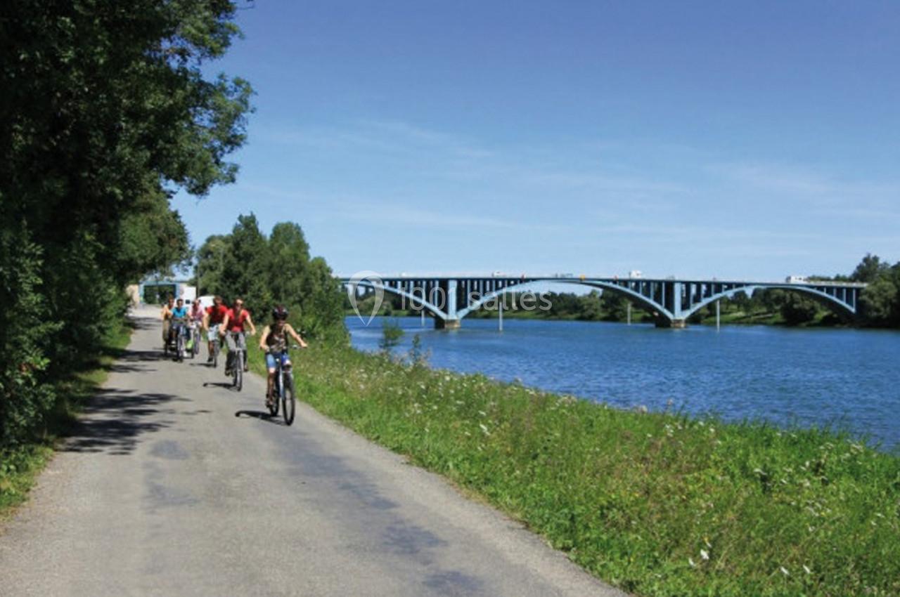 Un groupe de cyclistes roule sur une piste longeant une rivière avec un pont bleu visible à l'arrière-plan.