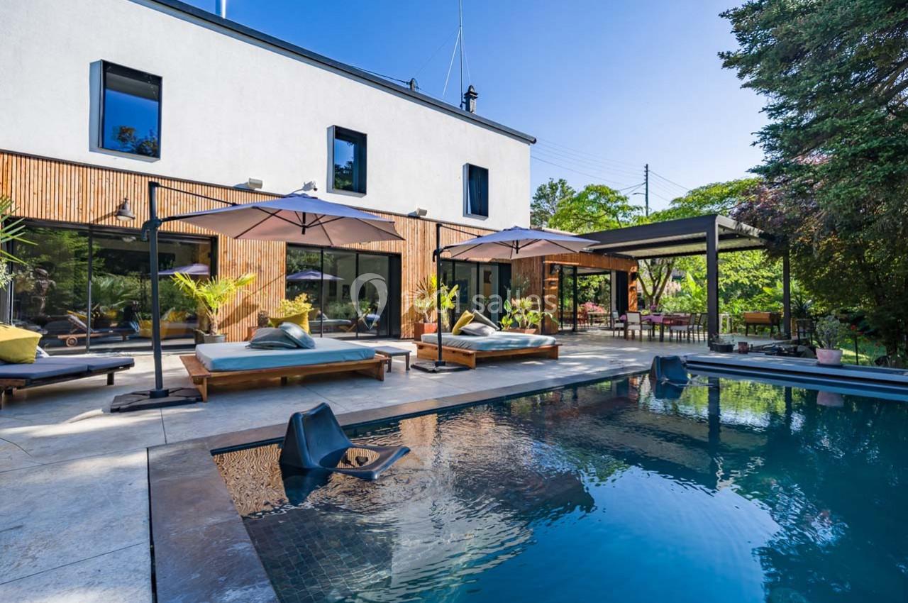 Terrasse moderne avec piscine, transats, parasols et végétation environnante devant une maison contemporaine.