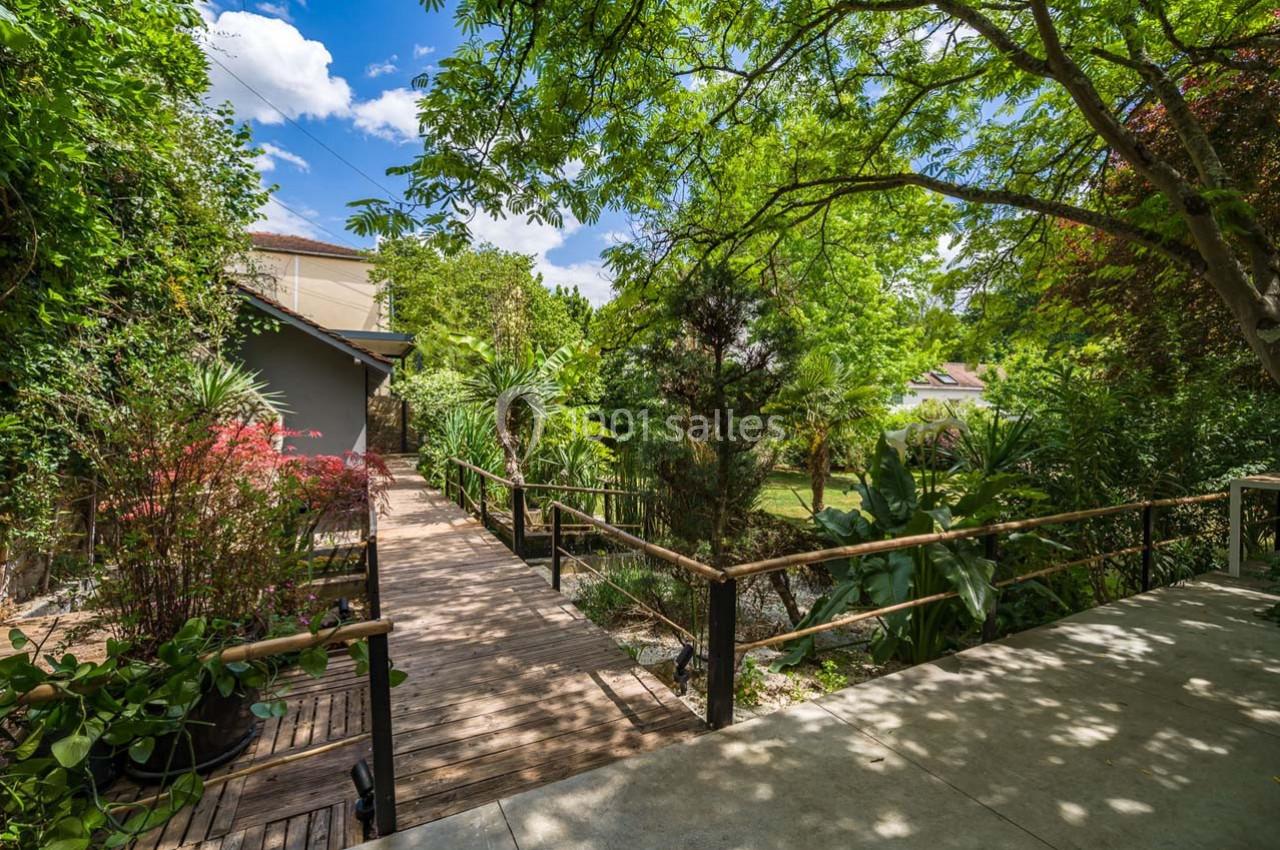 Passerelle en bois entourée de végétation luxuriante dans un jardin ensoleillé.