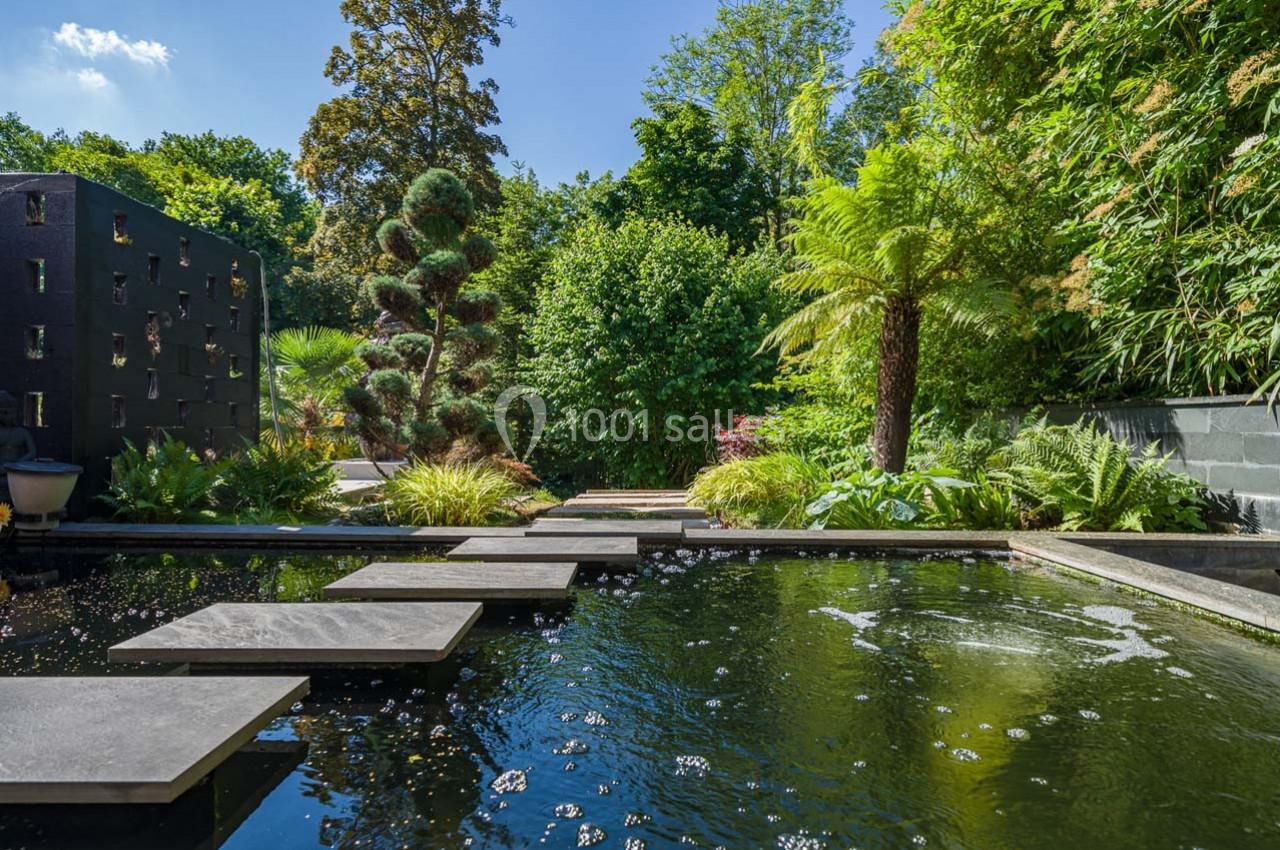 Étang avec des dalles en pierre formant un chemin, entouré de végétation luxuriante et d'arbres.