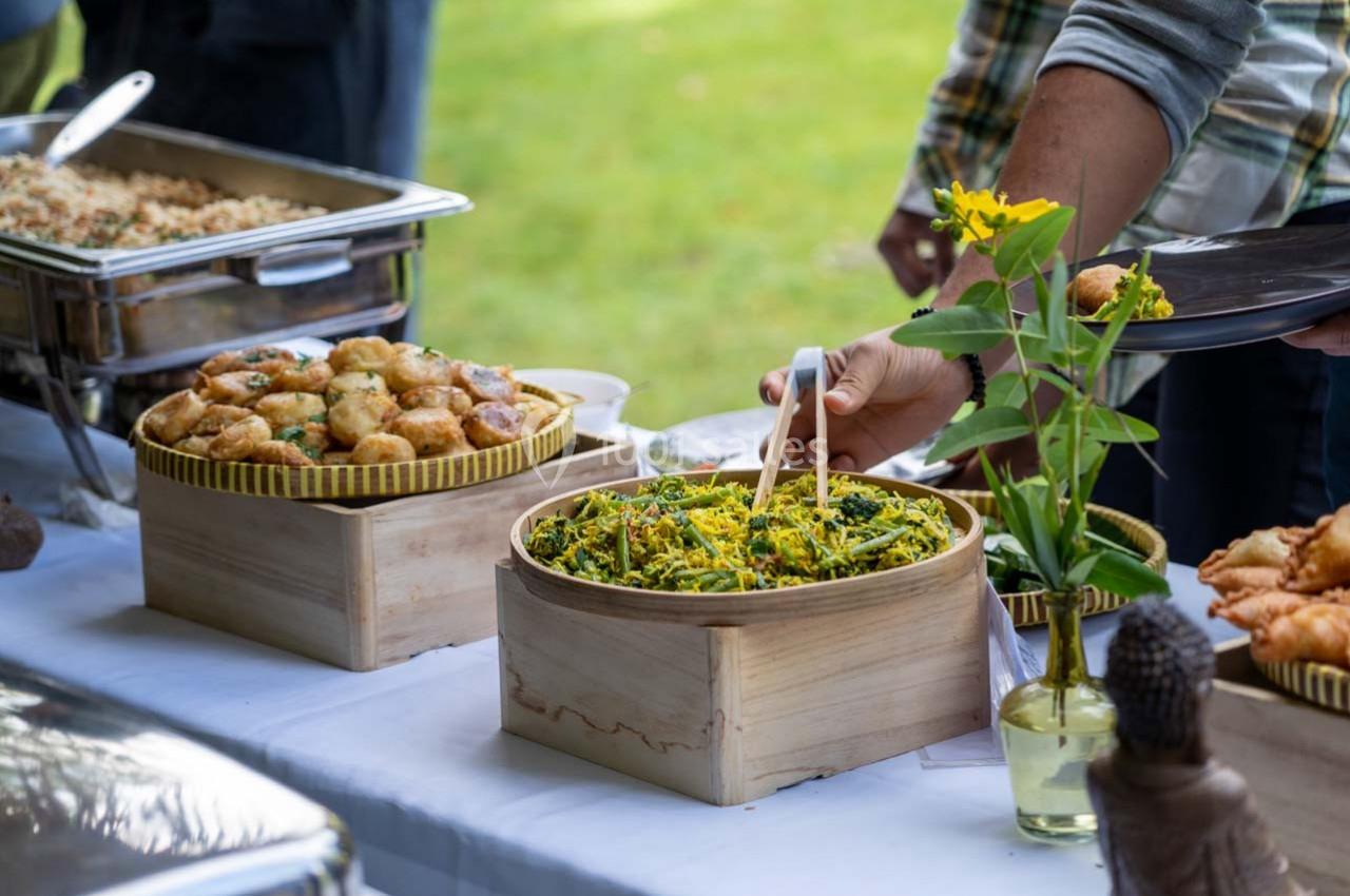 Buffet en plein air avec des plats variés, dont des salades et des beignets, sur une table blanche décorée de fleurs.