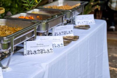 Un vase en verre avec des feuilles vertes posé sur une table dressée en extérieur, entourée de végétation.