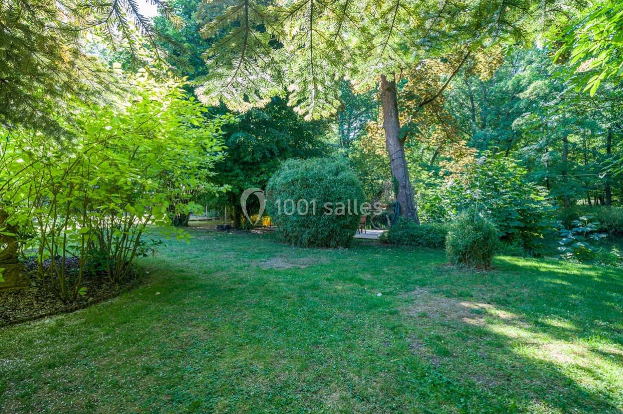 Pelouse verdoyante entourée d'arbres et de buissons dans un parc ensoleillé.