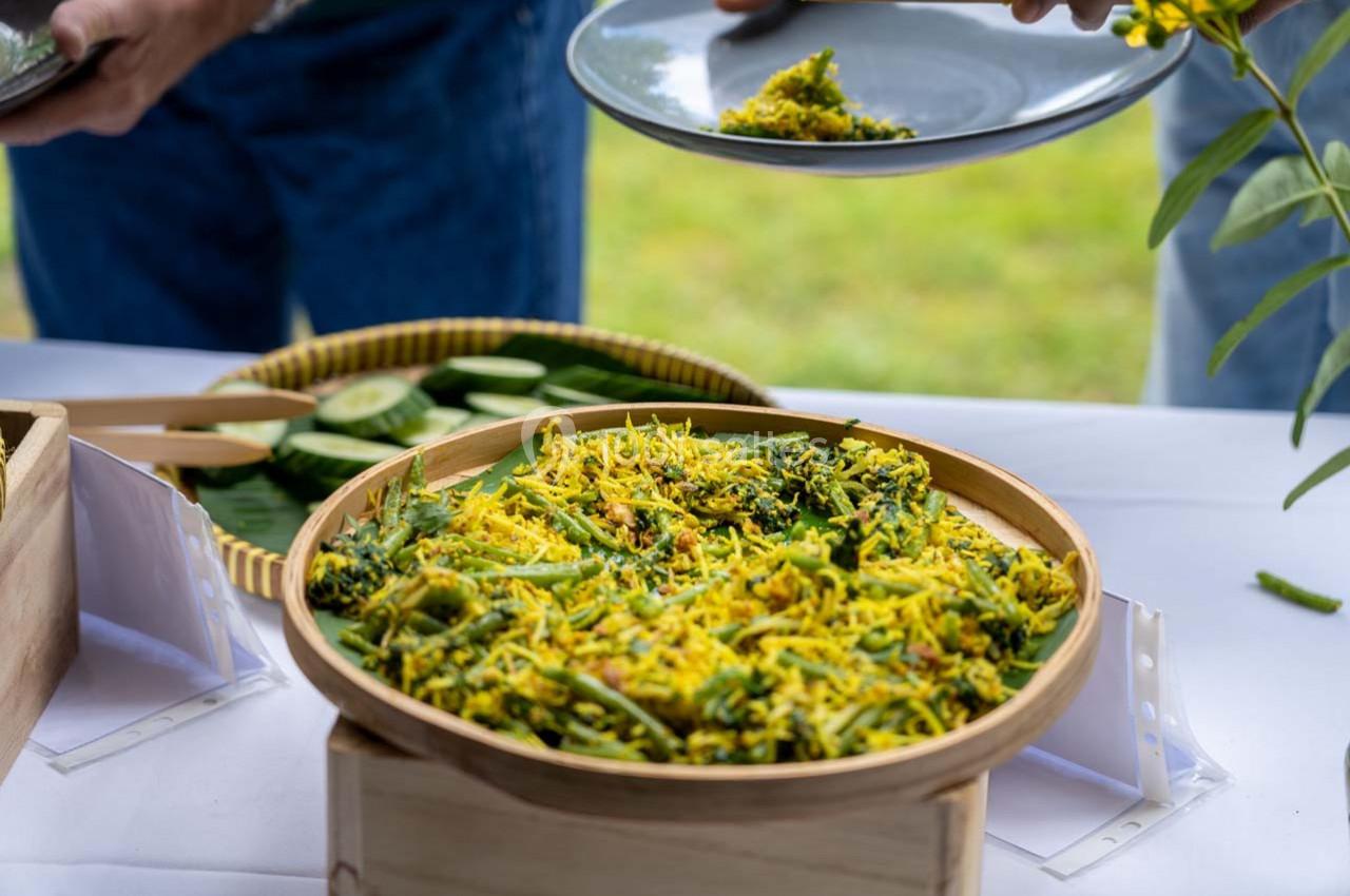 Un plat de salade colorée à base de légumes et d'herbes est servi dans un panier en bambou sur une table blanche.