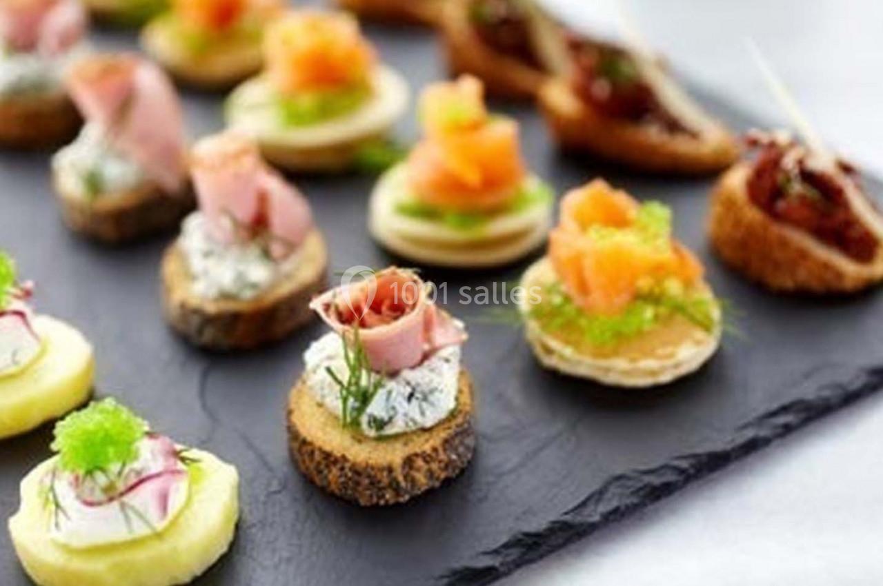 Assortiment de canapés variés avec garnitures de poisson, viande et légumes, disposés sur une ardoise noire.
