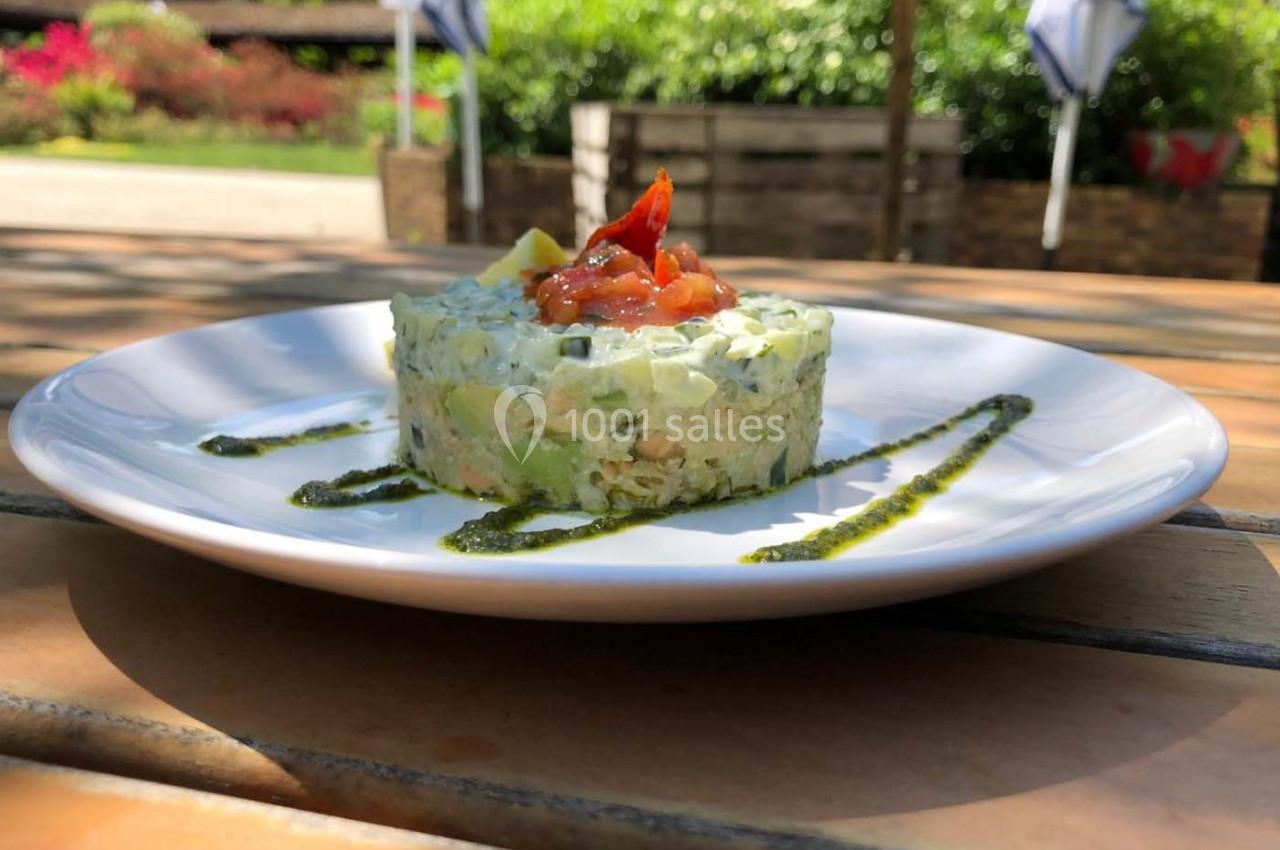 Tartare de légumes frais avec une garniture de tomates et avocat, servi sur une assiette blanche en extérieur.