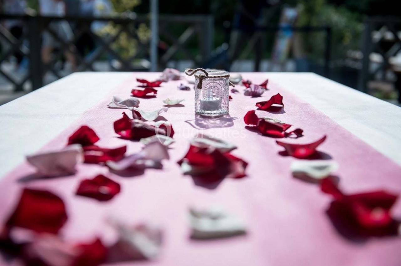 Pétales rouges et blancs dispersés sur une nappe rose avec une petite lanterne en verre au centre.