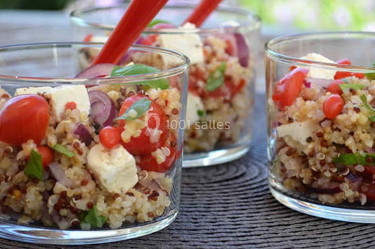 Verrines de salade de quinoa garnies de tomates cerises, feta, oignons rouges et herbes fraîches, avec des cuillères rouges.