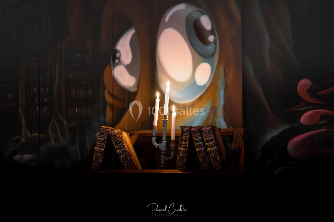 Un chandelier allumé et des livres anciens posés sur un pupitre en bois, avec une fresque colorée en arrière-plan.