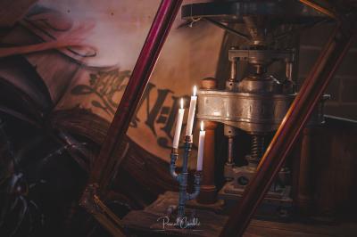 Un chandelier avec des bougies allumées posé près d'une ancienne presse métallique dans un décor artistique.