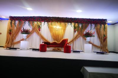 Salle de réception décorée avec des tables dressées, des ballons noirs et dorés, et des cordons rouges.