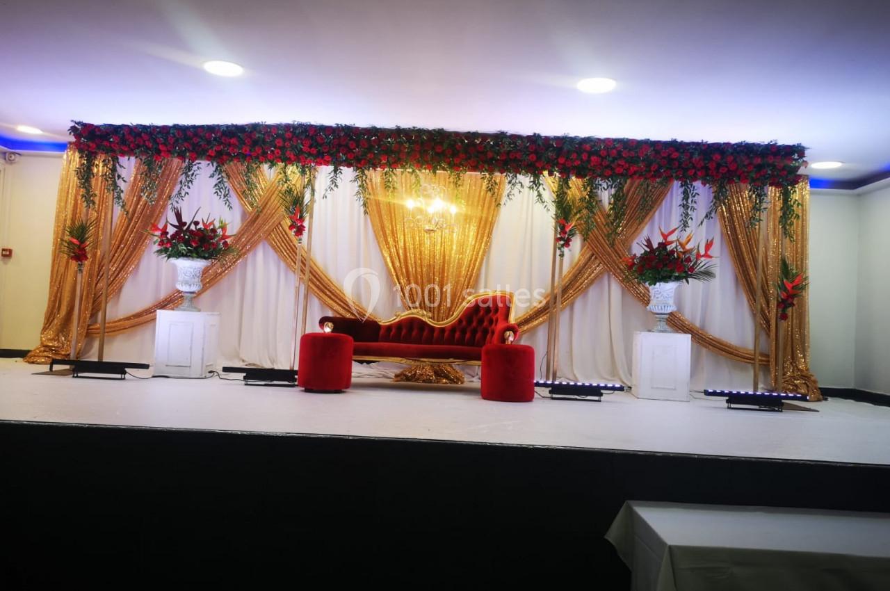 Décor de scène avec canapé rouge, rideaux dorés, fleurs rouges et blanches, éclairage chaleureux.