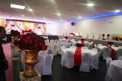 Salle de réception décorée avec des tables dressées, des ballons noirs et dorés, et des cordons rouges.