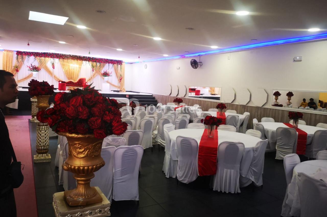 Salle de réception décorée avec des tables rondes, nappes blanches, chemins de table rouges et arrangements floraux rouges.