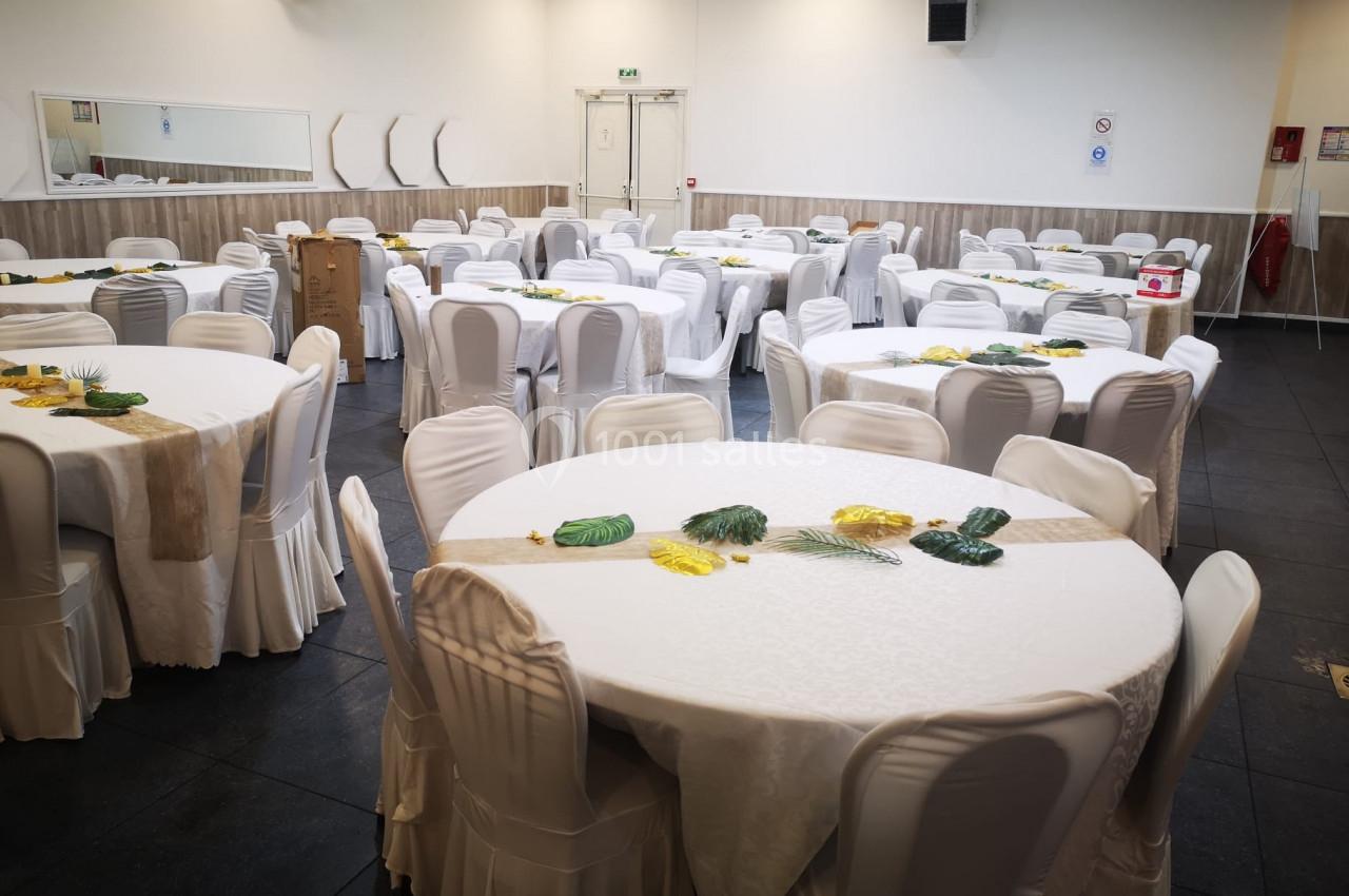Salle de réception avec des tables rondes dressées de nappes blanches et décorées de feuilles tropicales.