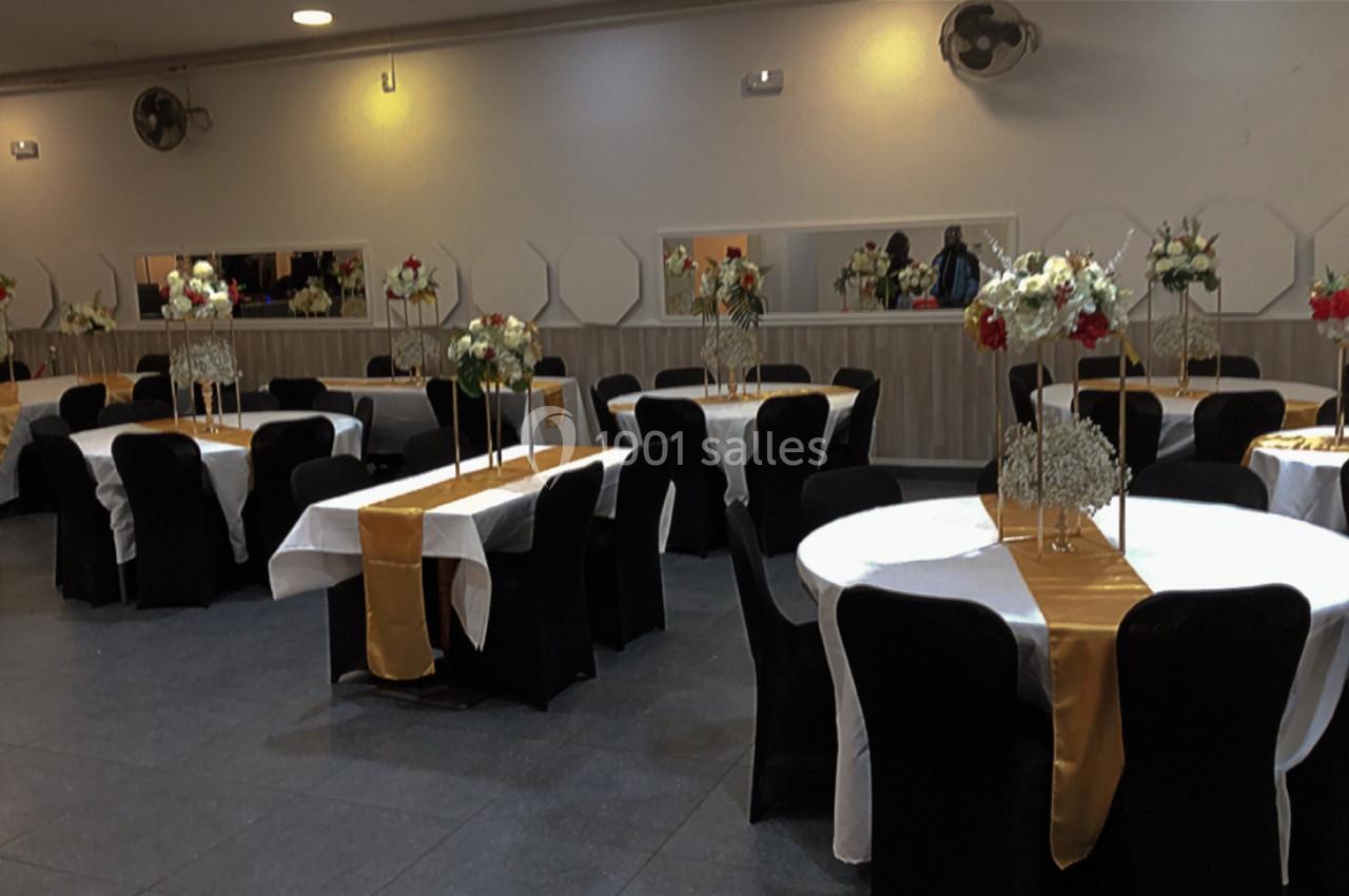 Salle de réception décorée avec des tables rondes, nappes blanches, chemins de table dorés et compositions florales.