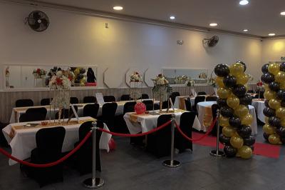 Salle de réception décorée avec des tables dressées, des ballons noirs et dorés, et des cordons rouges.