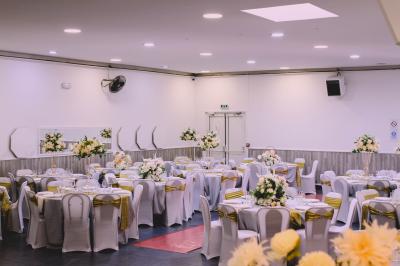 Salle de réception décorée avec des tables dressées, des ballons noirs et dorés, et des cordons rouges.