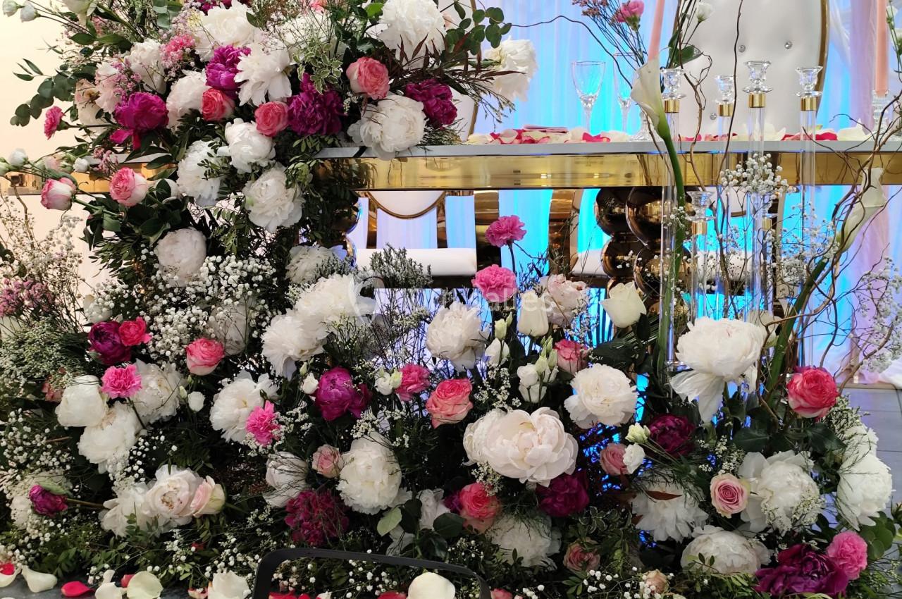 Arrangement floral coloré avec des roses blanches, roses et fuchsia, devant une table décorée pour une réception.