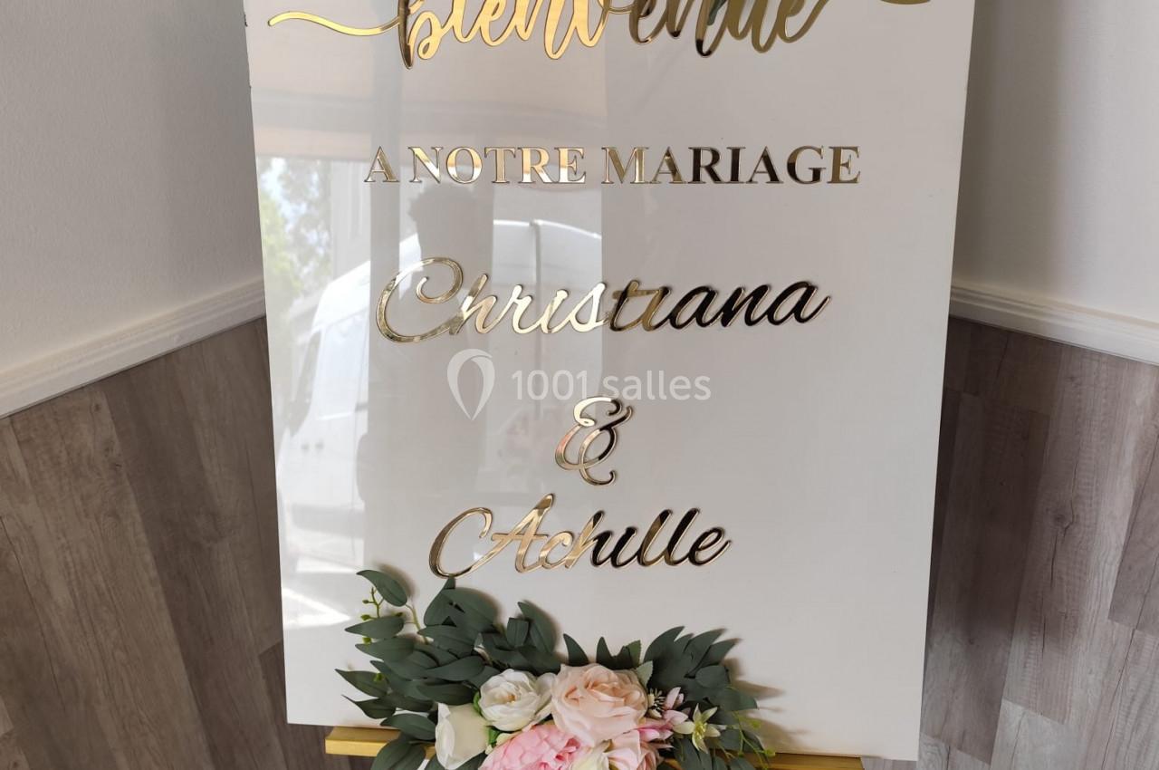 Panneau blanc décoré de fleurs roses et feuillages, portant l'inscription ’Bienvenue à notre mariage’.