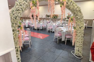 Salle de réception décorée avec des tables dressées, des ballons noirs et dorés, et des cordons rouges.