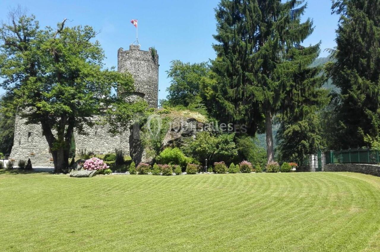 Château en pierre entouré d'arbres et de pelouses bien entretenues, avec un drapeau au sommet de la tour.