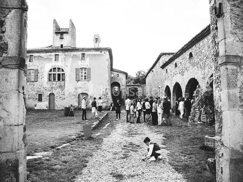 Un groupe de personnes rassemblées dans la cour d'un bâtiment en pierre ancienne, avec un enfant accroupi au premier plan.