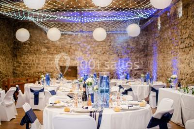 Salle en pierre avec tables rondes dressées pour un événement, décorée de lanternes suspendues et de fleurs.