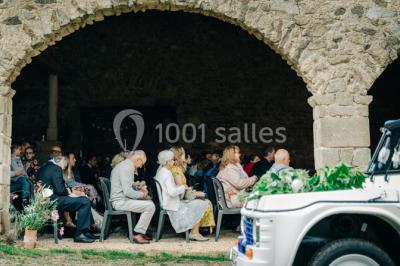 Salle en pierre avec tables rondes dressées pour un événement, décorée de lanternes suspendues et de fleurs.