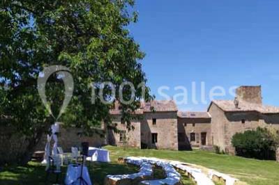 Salle en pierre avec tables rondes dressées pour un événement, décorée de lanternes suspendues et de fleurs.