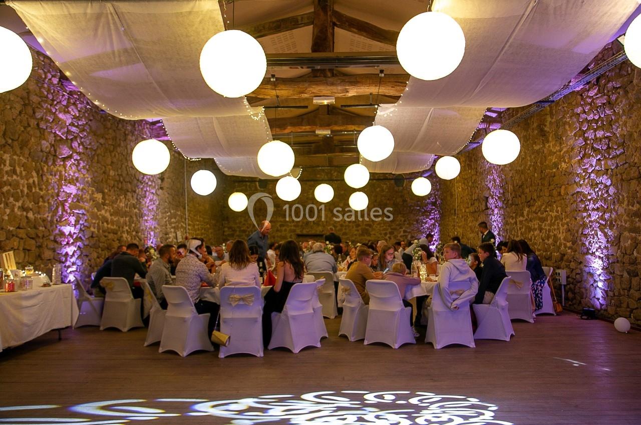 Salle en pierre décorée de guirlandes lumineuses et de lanternes, avec des invités assis à des tables rondes.