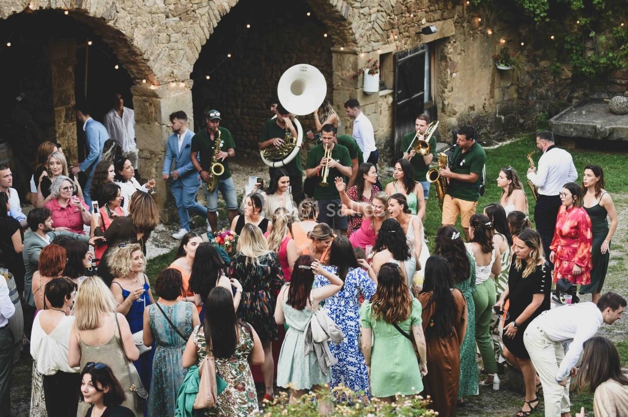 Groupe de personnes dans une cour en pierre, écoutant un orchestre de cuivres lors d'une fête en plein air.