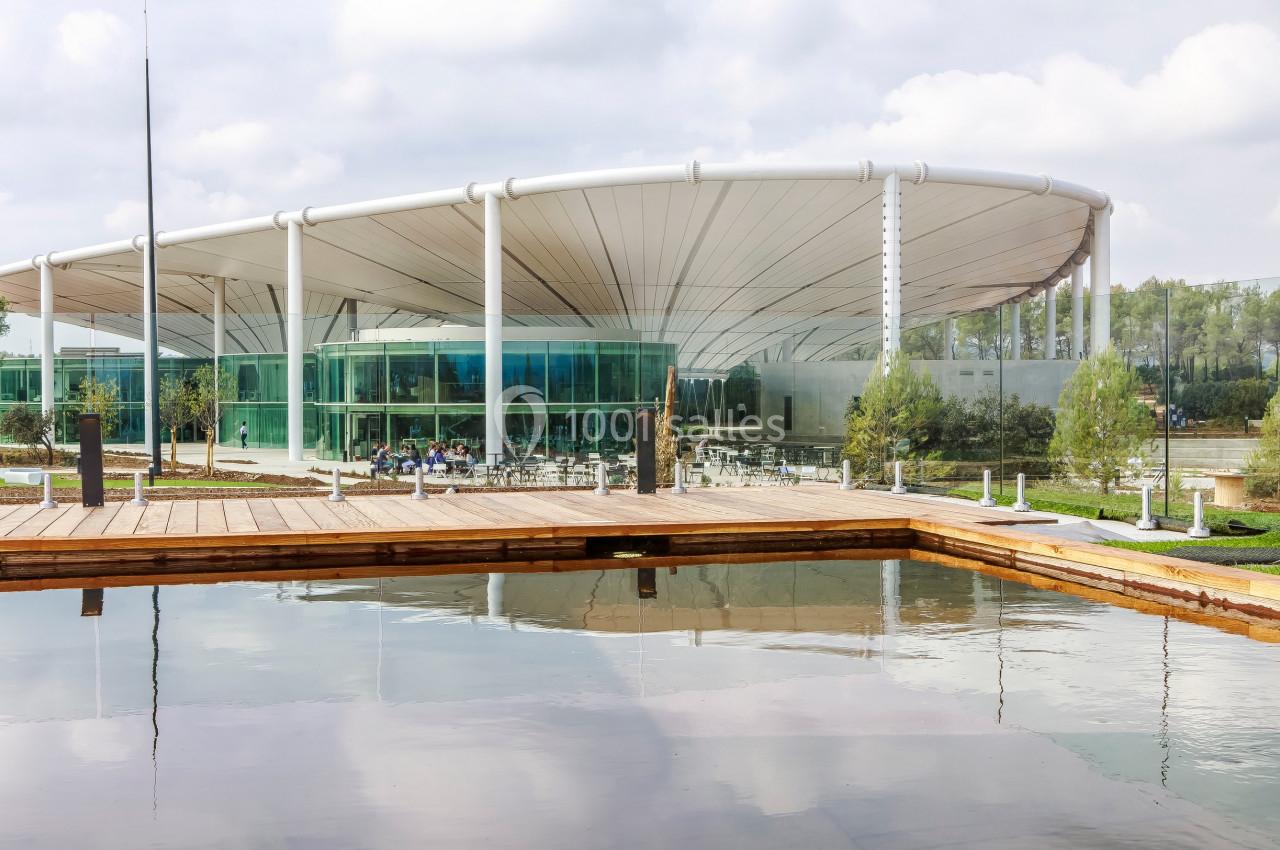 Bâtiment moderne avec une structure circulaire vitrée, entouré d'un bassin et d'espaces verts.