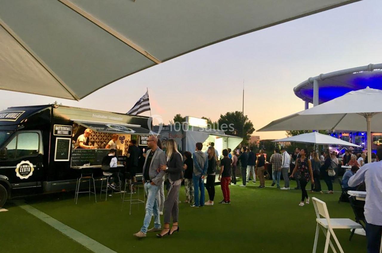 Des personnes rassemblées autour de food trucks sur une pelouse, sous des parasols, en soirée.