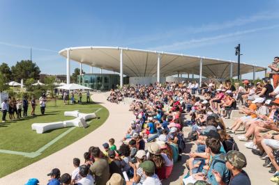 Bâtiment moderne avec une structure en toit incurvé, entouré de végétation et éclairé au crépuscule.