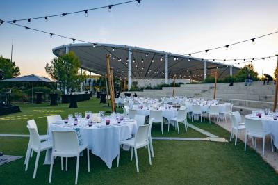 Bâtiment moderne avec une structure en toit incurvé, entouré de végétation et éclairé au crépuscule.