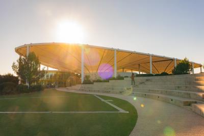 Bâtiment moderne avec une structure en toit incurvé, entouré de végétation et éclairé au crépuscule.