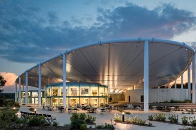 Bâtiment moderne avec une structure en toit incurvé, entouré de végétation et éclairé au crépuscule.