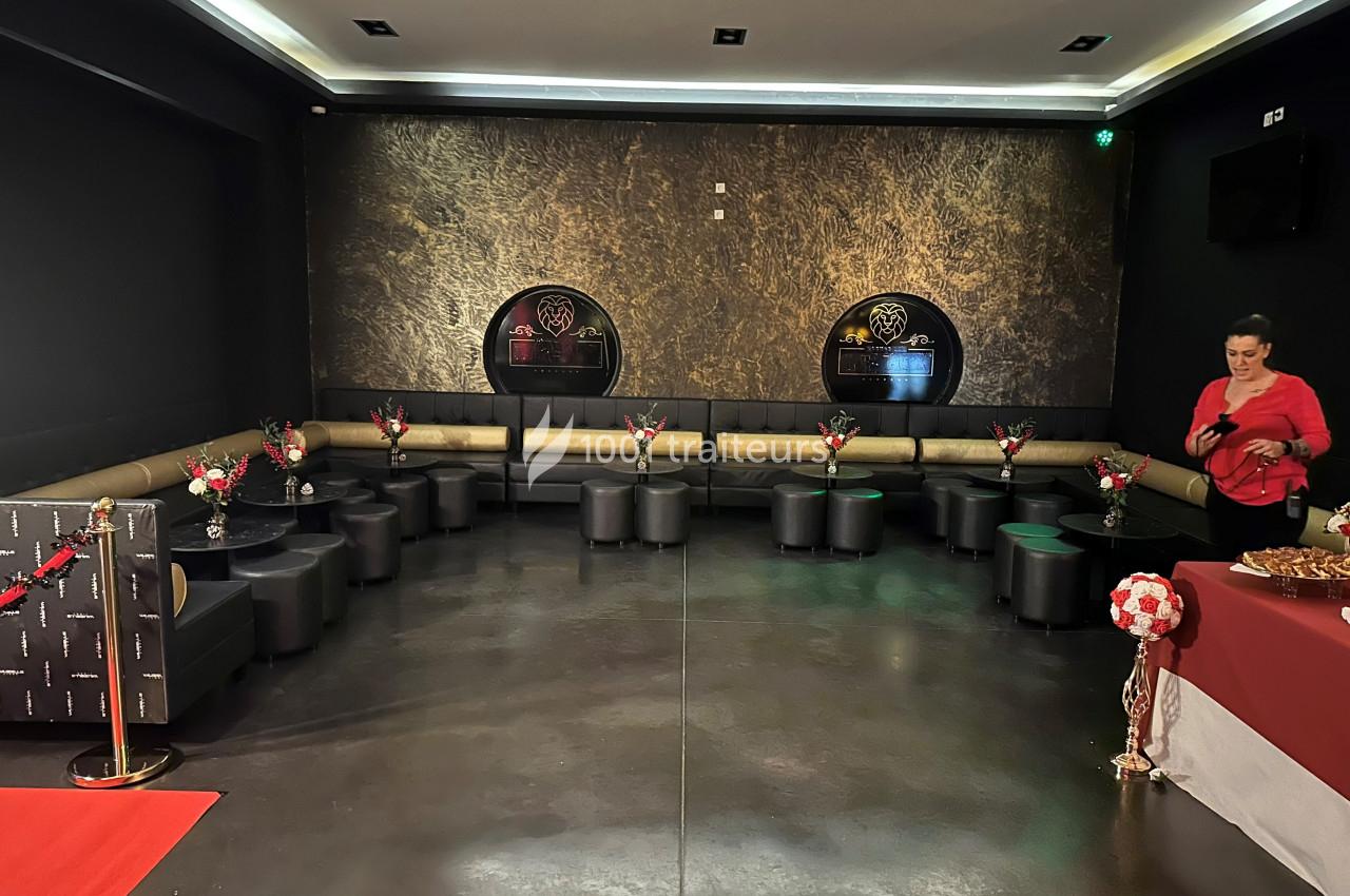 Salle de réception avec banquettes noires, tables basses décorées de fleurs et buffet sur la droite.