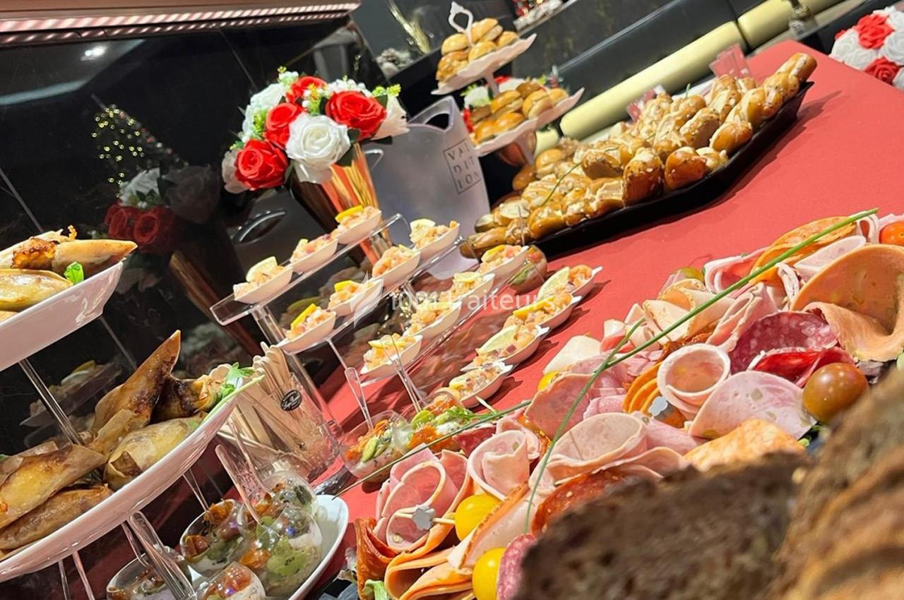 Buffet varié avec charcuterie, amuse-bouches, pains et décorations florales sur une table rouge.