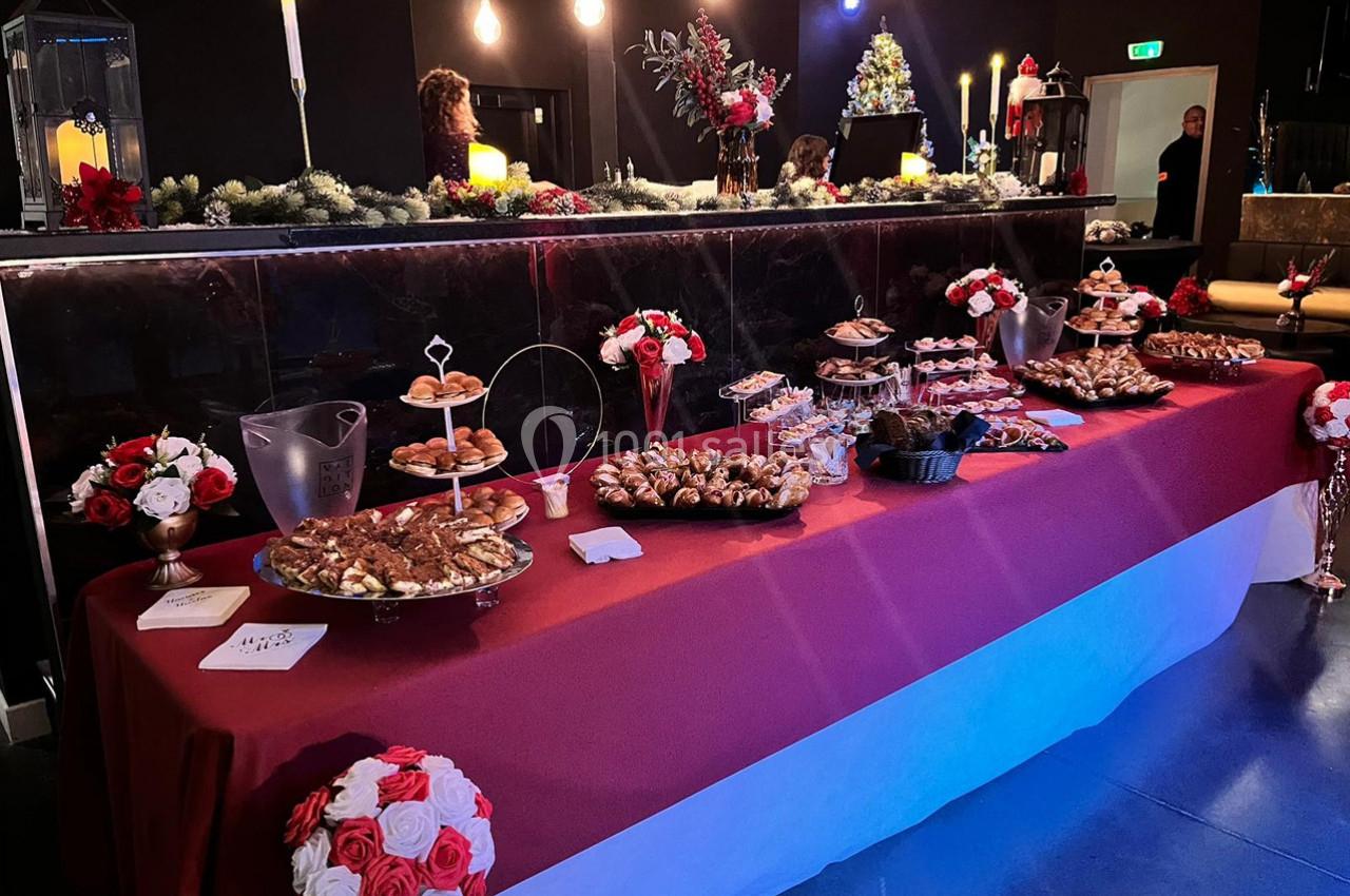 Table garnie de pâtisseries et desserts variés dans un décor festif avec guirlandes et bougies.